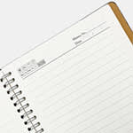 A spiral notebook with a white paper interior and a brown cover, featuring metal spiral binding.
