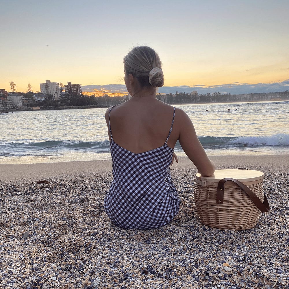 A wicker cooler basket in a natural finish, featuring a woman pouring a drink into a glass beside it.