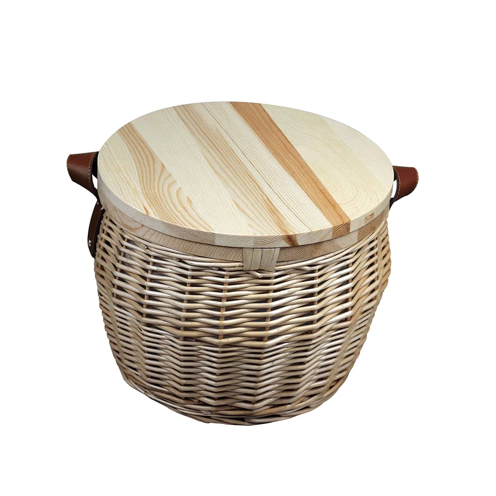 A wicker cooler basket in natural colour with a leather strap, resting on a beach blanket, with a glass of wine beside it.