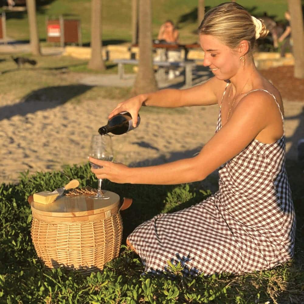 A wicker cooler basket with a wooden lid and leather handles, featuring a natural colour scheme.