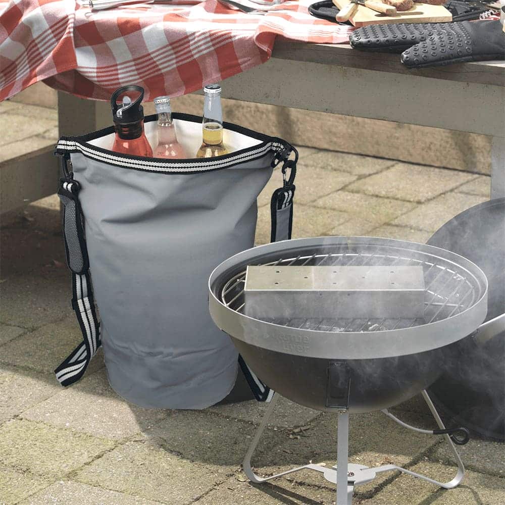 A grey waterproof cooler backpack with straps, placed near a barbecue, holding drink bottles. It has a logo.