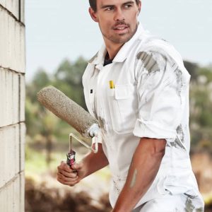A man in a white cotton drill overall stands with a paint roller, set against a blurred outdoor background.