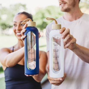A drink bottle featuring a clear body, measuring indicators, a wooden lid, and available in navy blue and white.