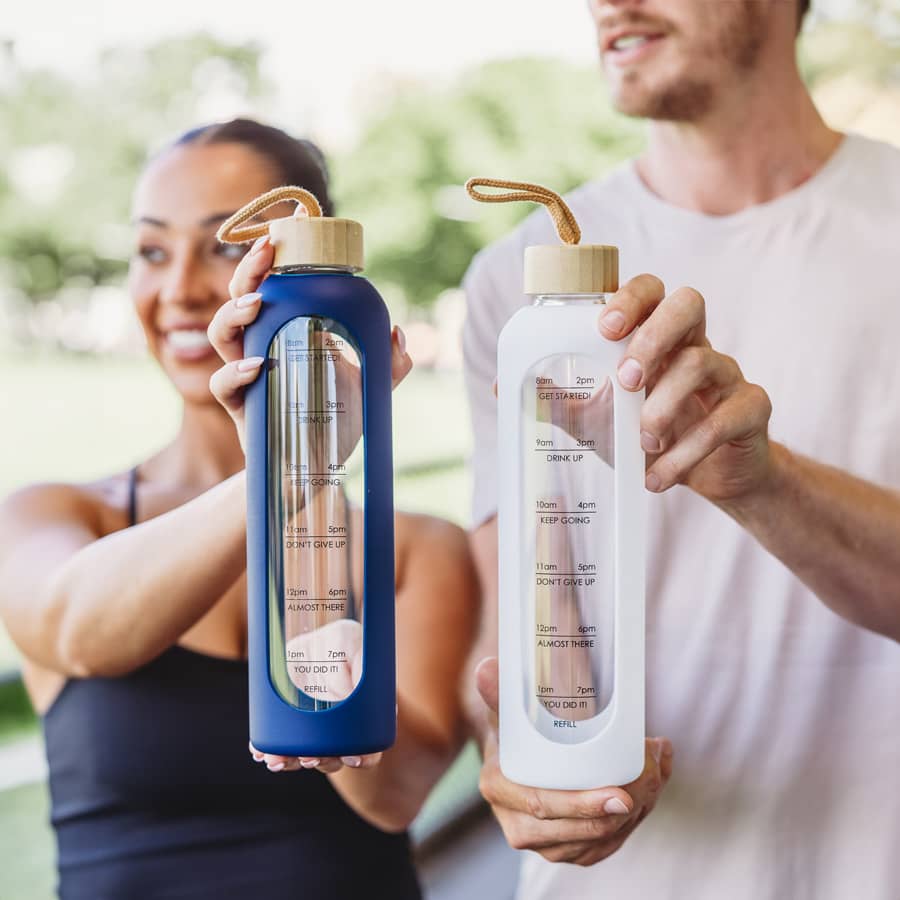 A drink bottle featuring a clear body, measuring indicators, a wooden lid, and available in navy blue and white.