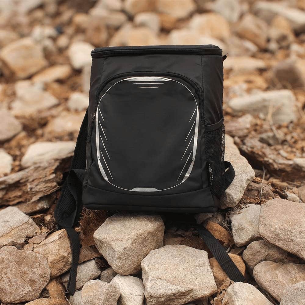 A black cooler backpack with a front pocket and mesh side pockets, set against a rocky background.