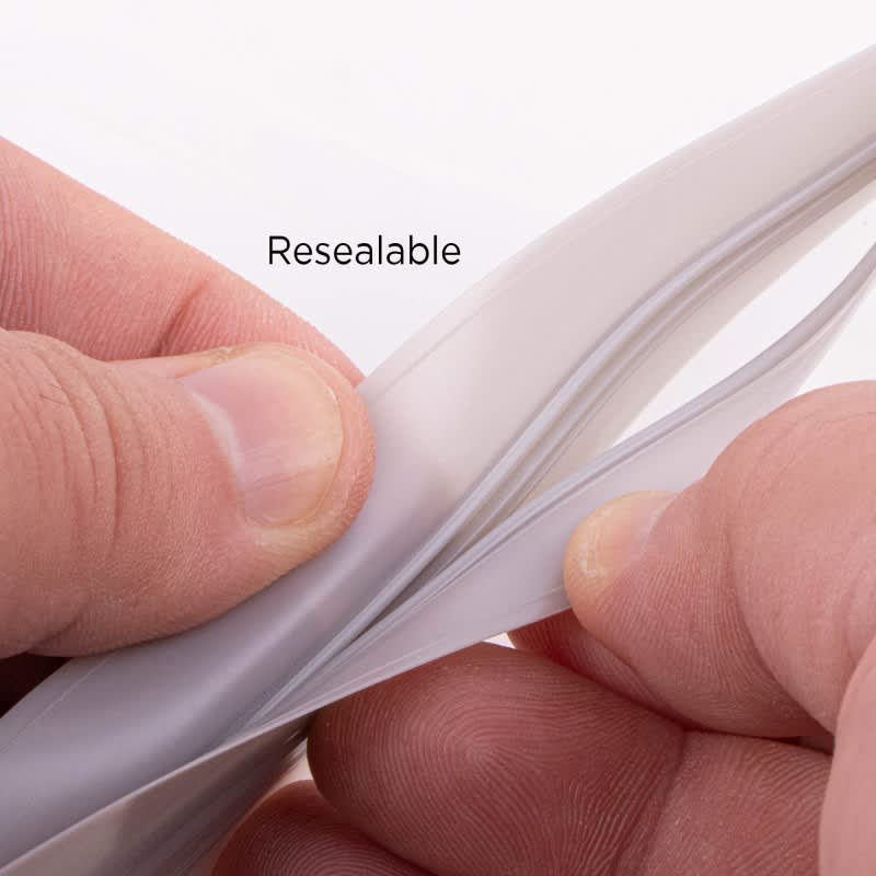 A hands holding a clear, resealable PEVA reusable food storage bag, showcasing its seal and material texture.