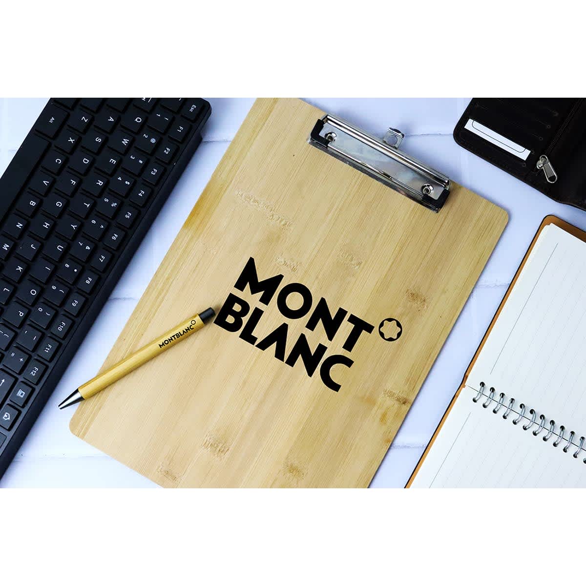 A bamboo clipboard with a clipboard clip, featuring a logo, placed on a desk with a keyboard and notebook.