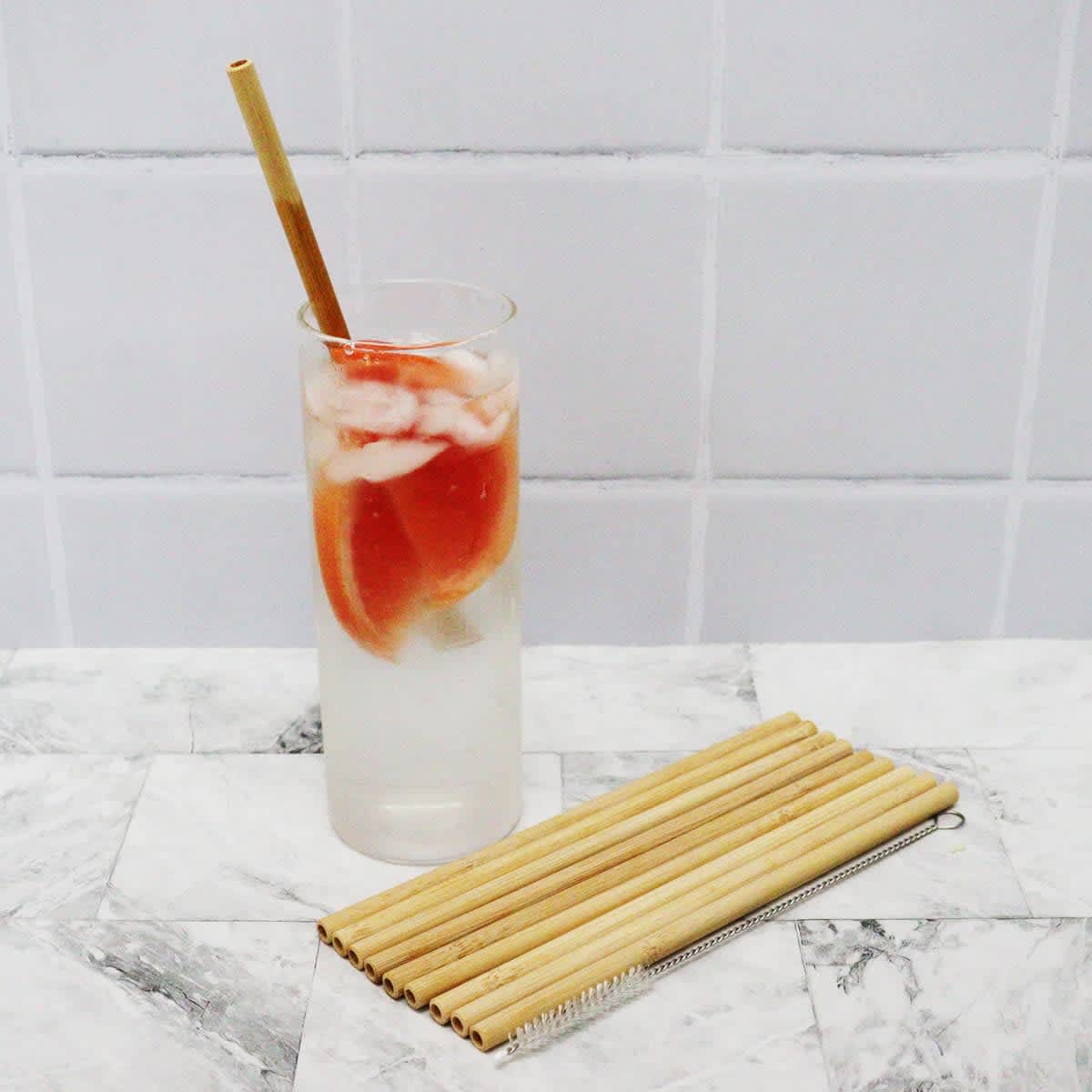 A drink bottle filled with a fruity beverage and ice, accompanied by ten bamboo straws in natural colour.