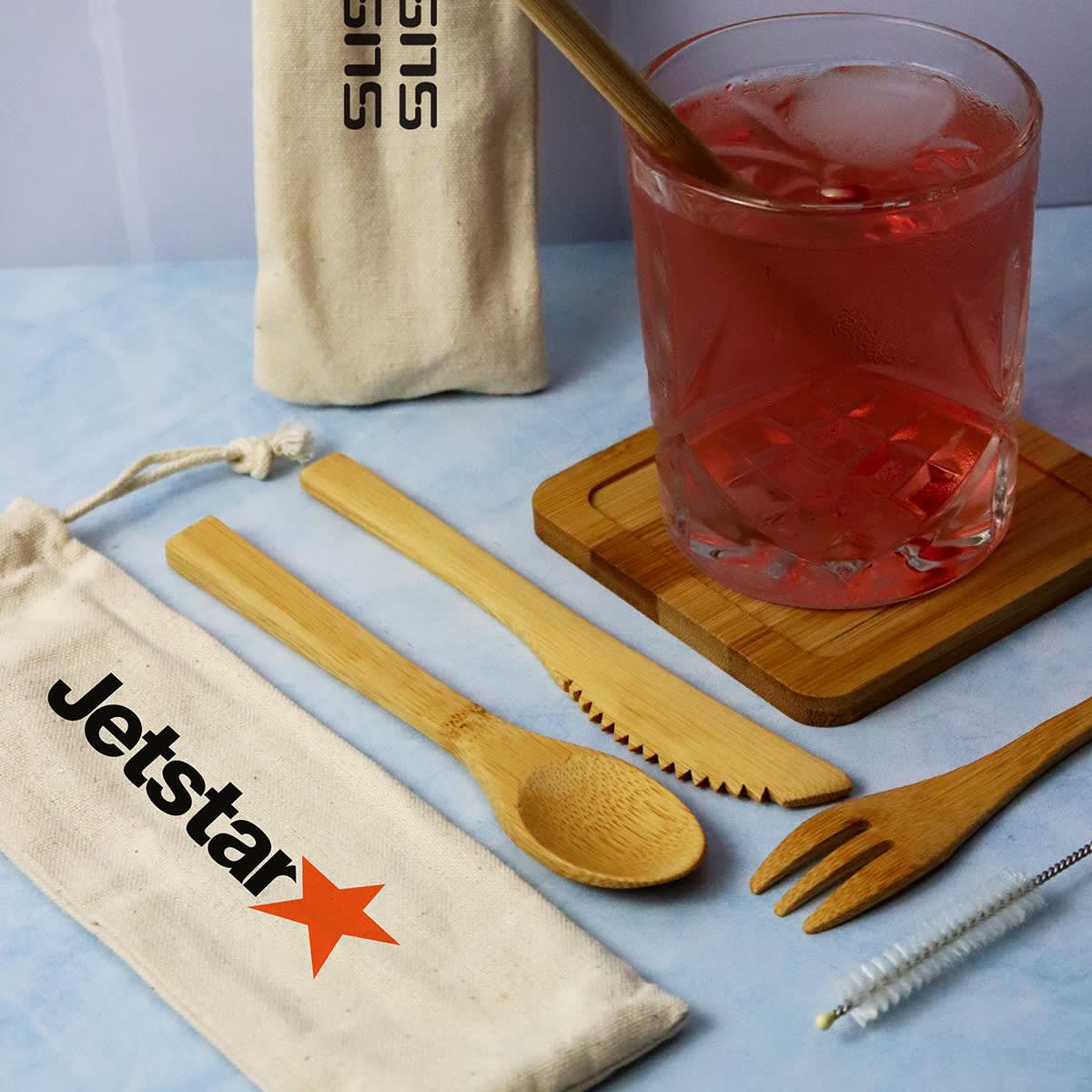 A bamboo cutlery set including a fork, spoon, knife, and cleaning brush, with a drawstring pouch and a drink glass.