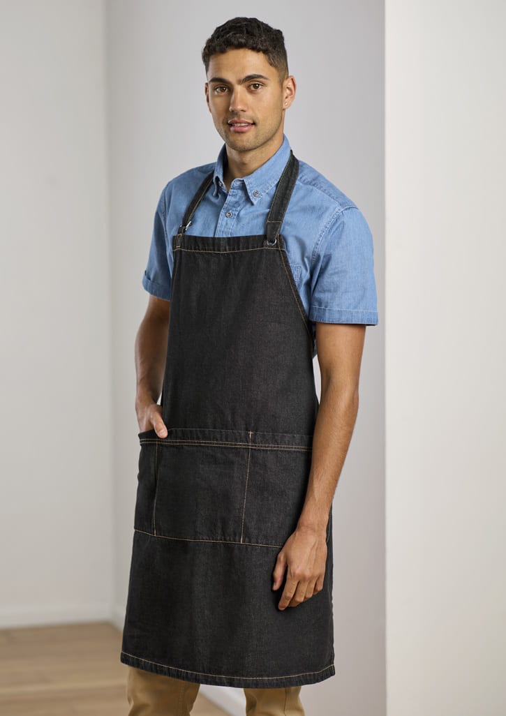 A man wearing a dark denim apron over a blue shirt, featuring pockets and adjustable straps.