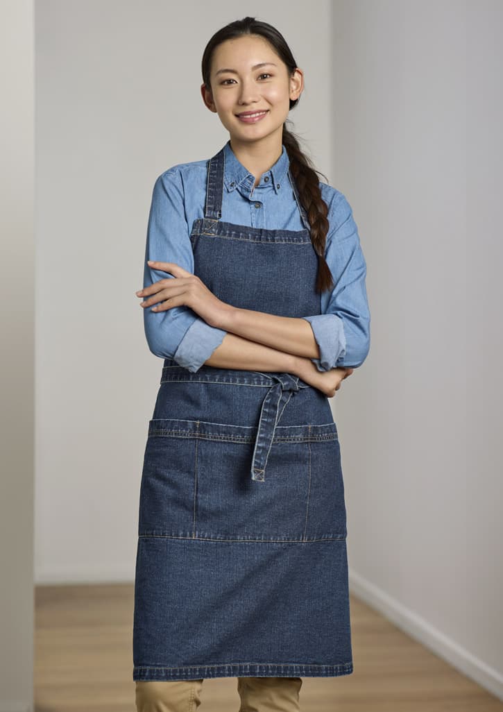 A denim apron with a fitted design, worn over a blue shirt, featuring a logo and front pockets.