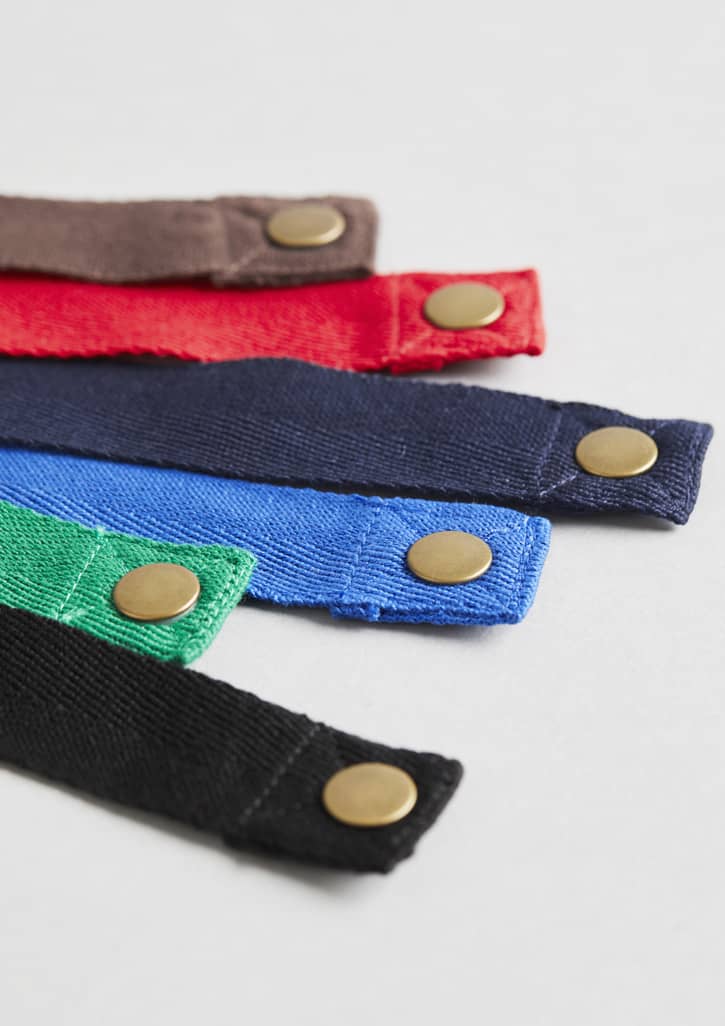 A selection of Urban Bib Straps in red, blue, green, black, and brown, featuring brass snaps.