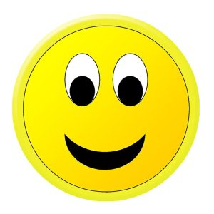 A yellow 44mm button badge featuring a smiling face with large eyes and a friendly expression. It has a logo in the corner.