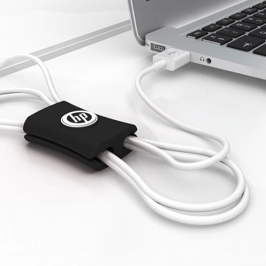 A black cable manager with a logo, organising white cables connected to a laptop on a white surface.