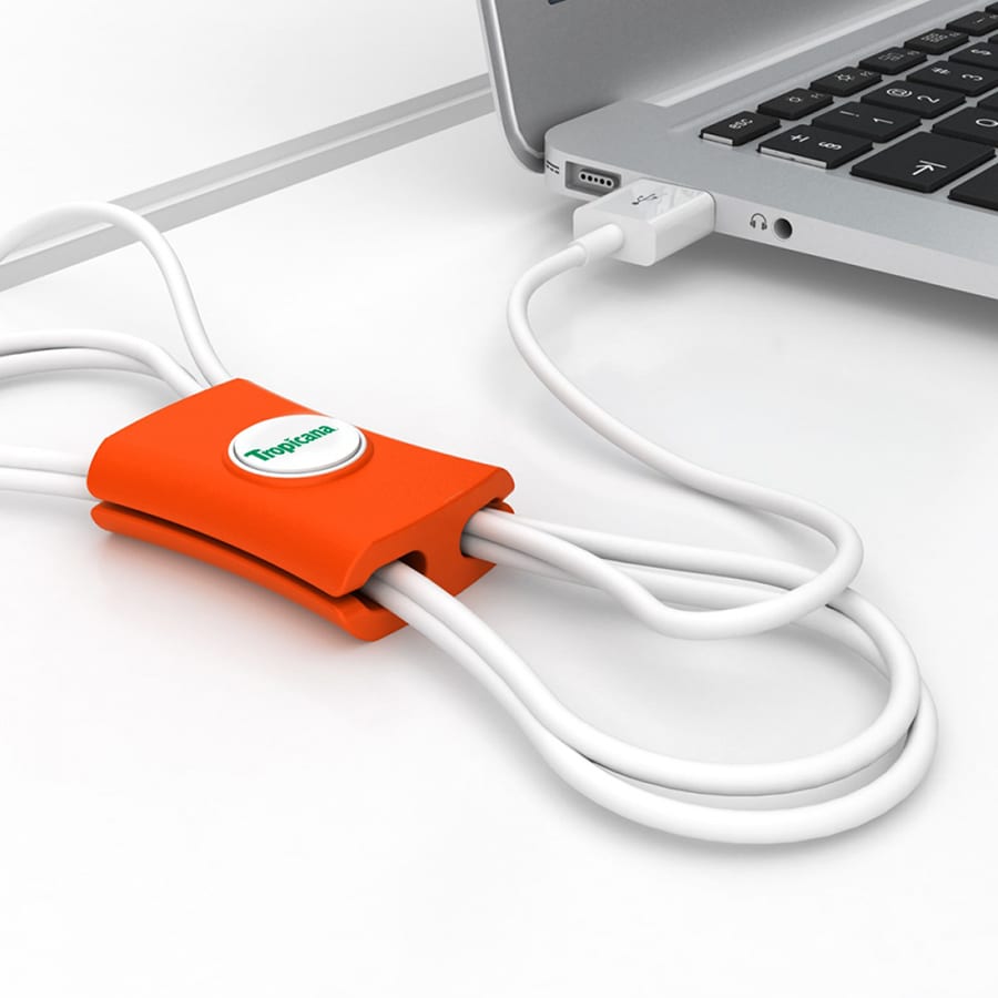 An orange cable manager with a logo, holding white cables neatly beside a laptop.