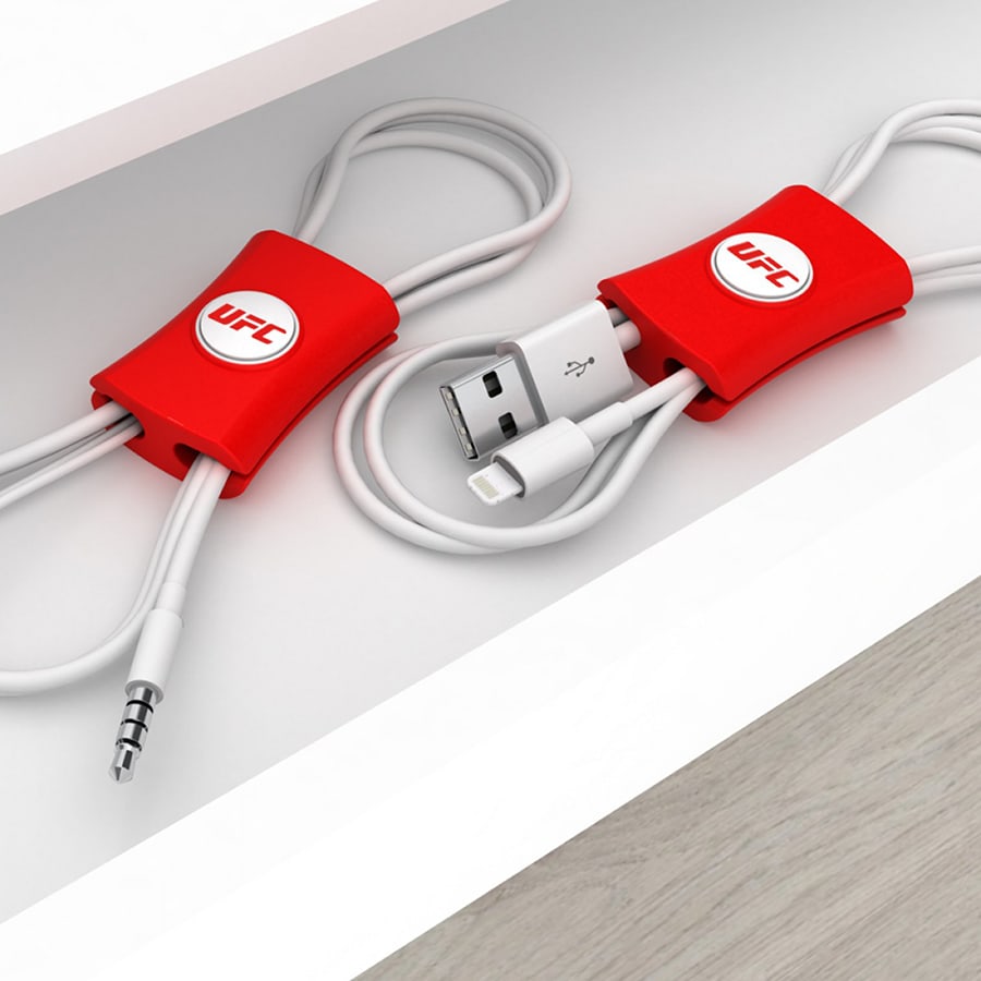 A red cable manager sits on a shelf, neatly organising two white cables, with a logo present on the product.