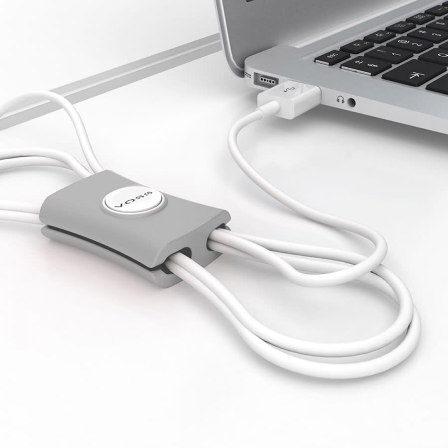A grey cable manager with multiple white cables attached, positioned next to a laptop. It features a logo.