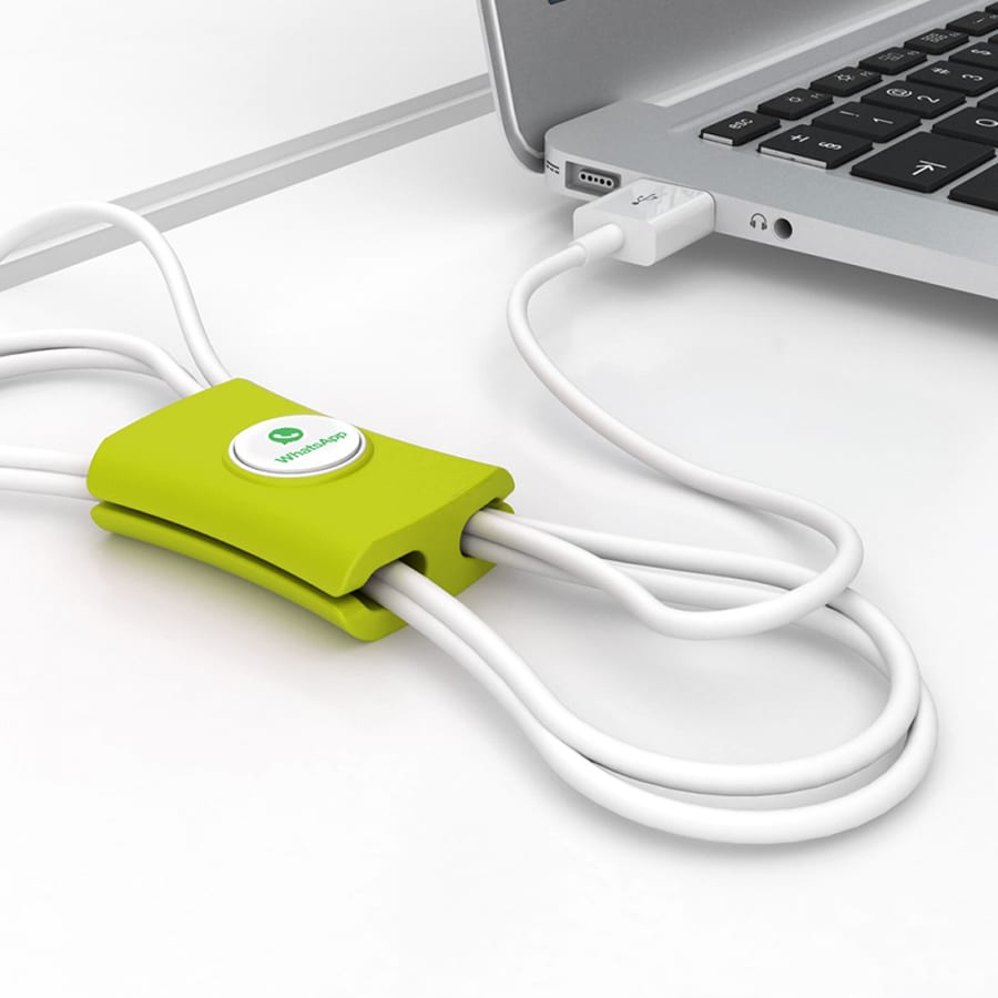 A green cable manager with multiple white cables attached, placed next to a laptop. It features a logo.