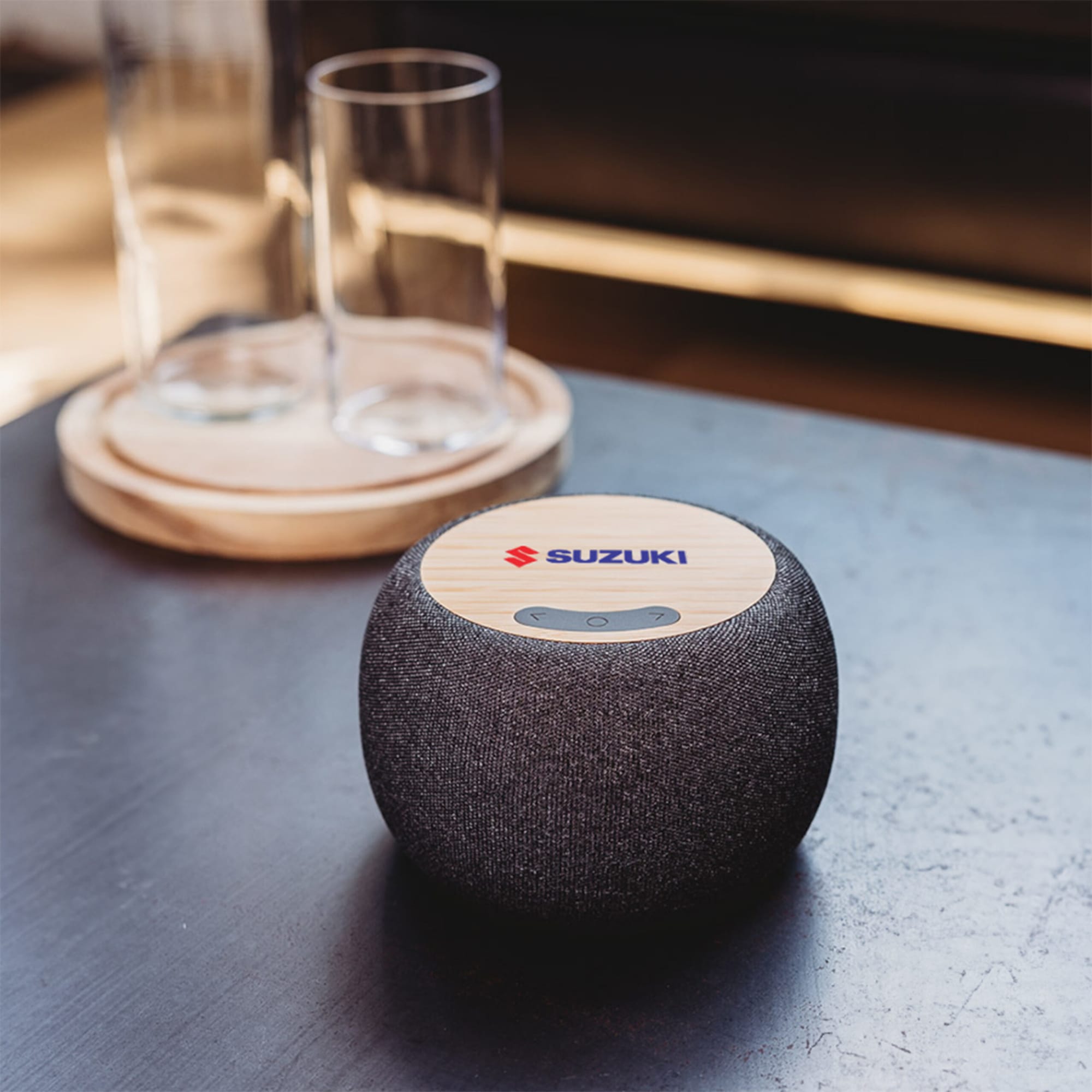 A wireless speaker with a bamboo top and a dark fabric body, featuring a logo on the top.