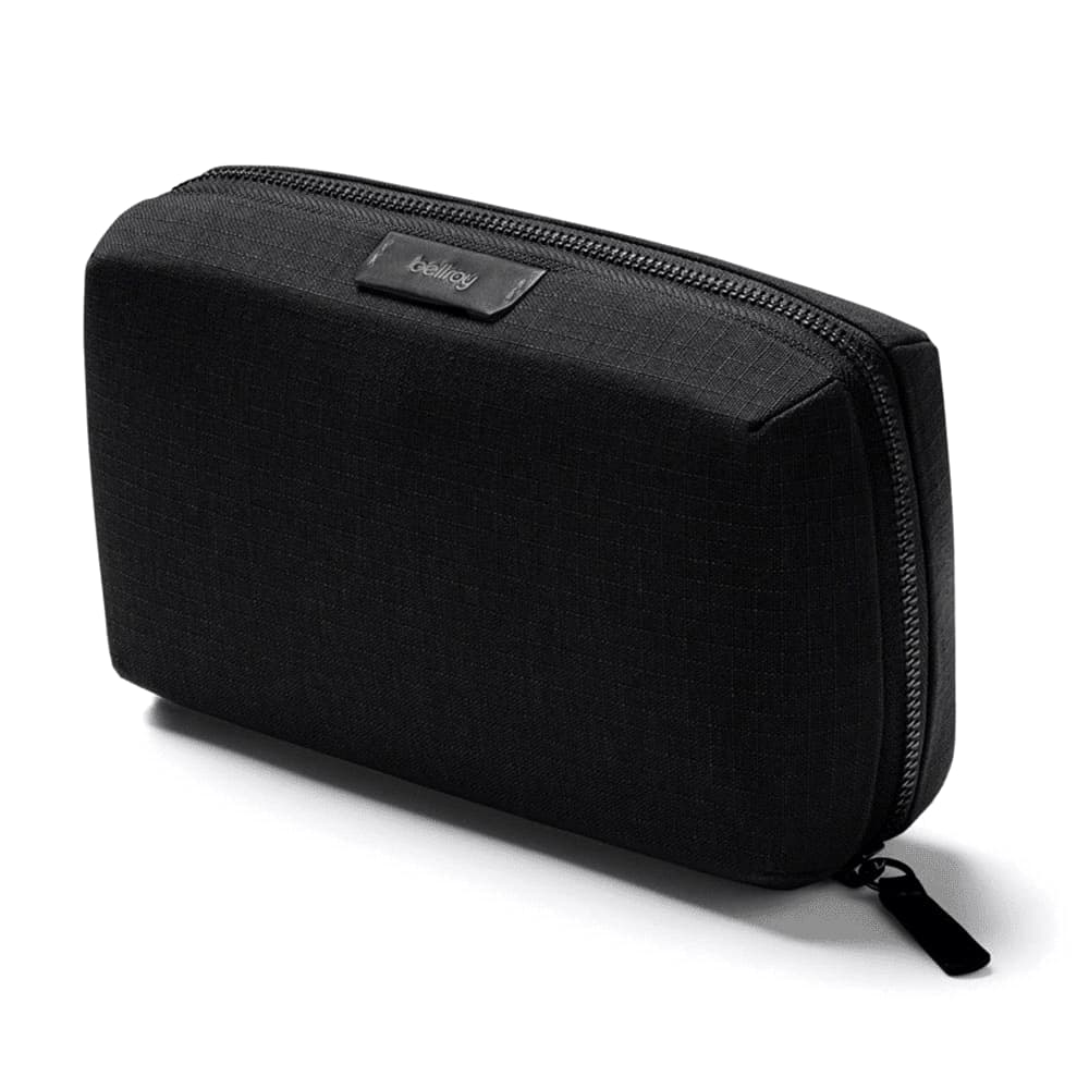 A black tech kit with compartments for cables, a mouse, and accessories, being held by a hand on a table.