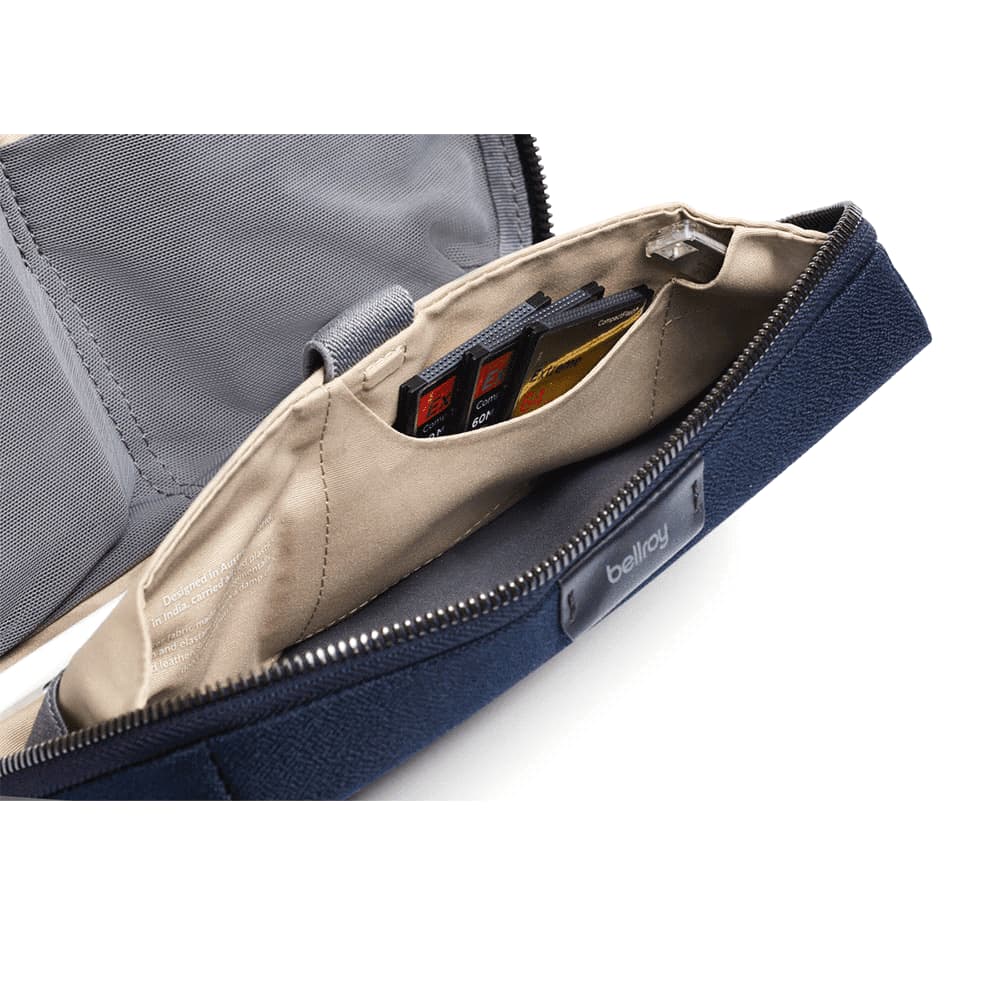 A navy tech kit containing a stylus, cables, and a case for earbuds, secured with elastic straps inside.