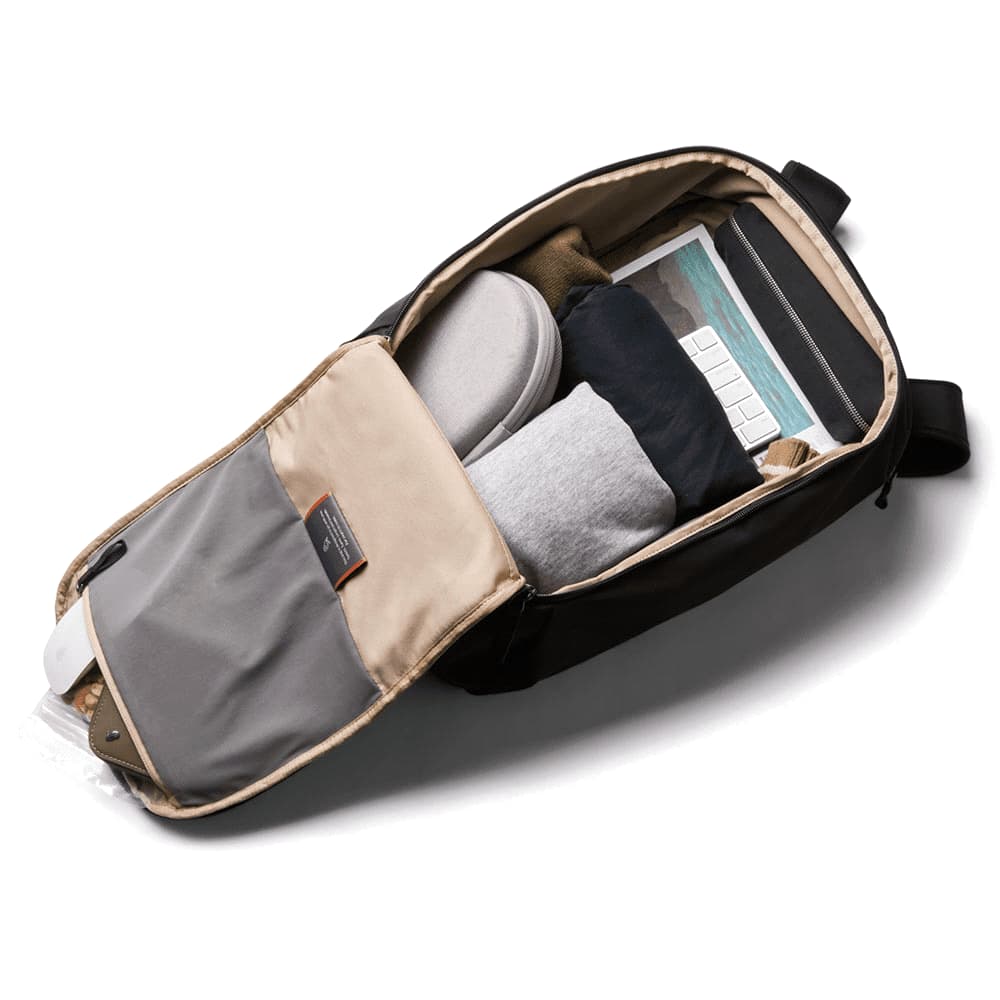 A black backpack partially unzipped, revealing neatly packed items including clothing, a laptop, and other accessories.