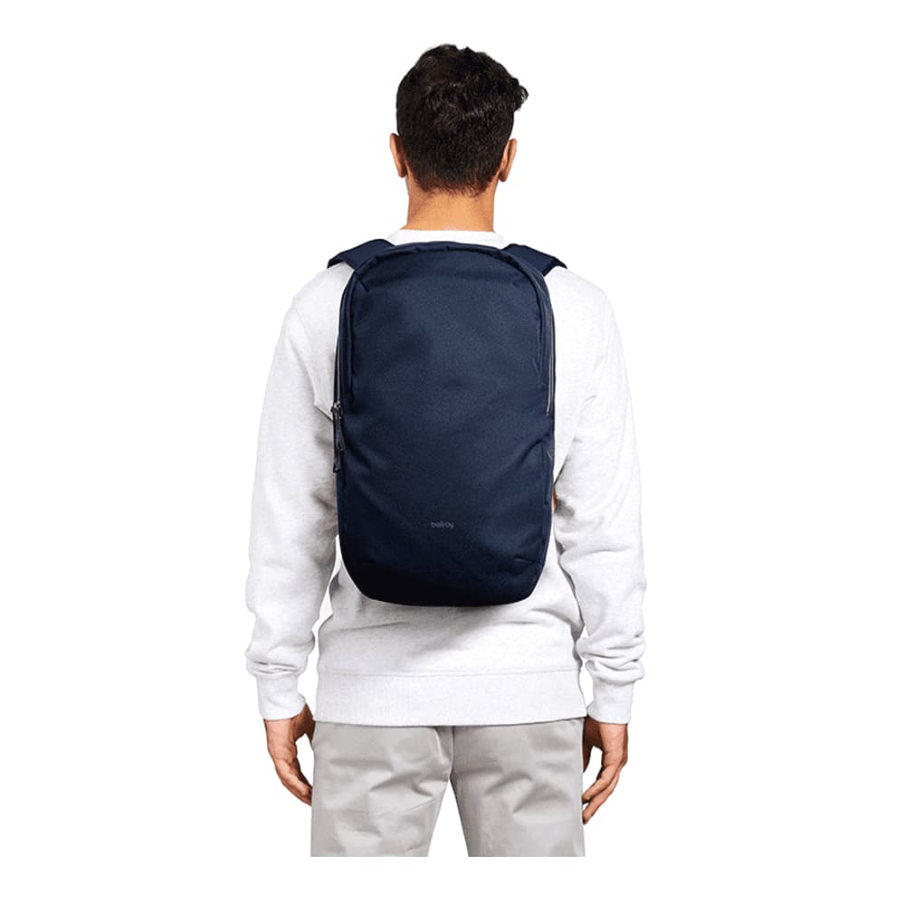 A black Bellroy Via Backpack 20L is worn on the back of a person in casual attire, showcasing its sleek design.