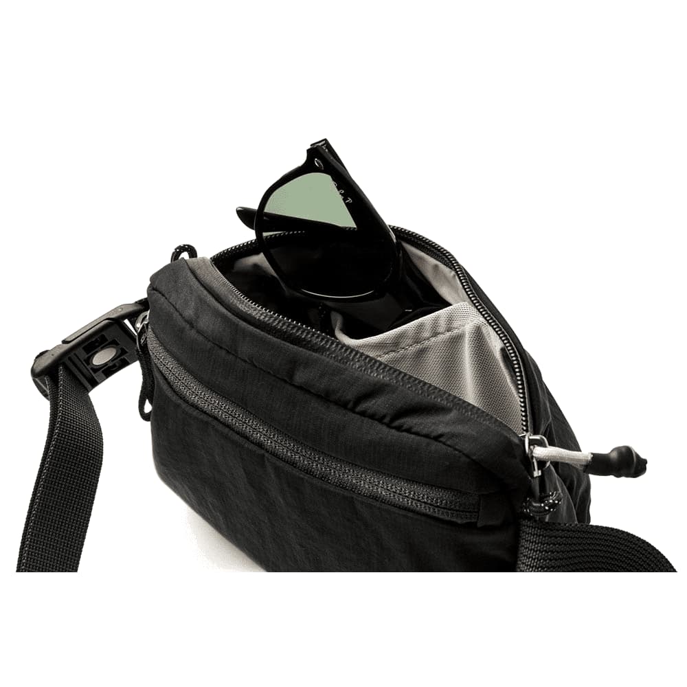 A black Bellroy Lite Belt Bag with an open zipper, revealing various items inside, including a drink bottle and an umbrella.