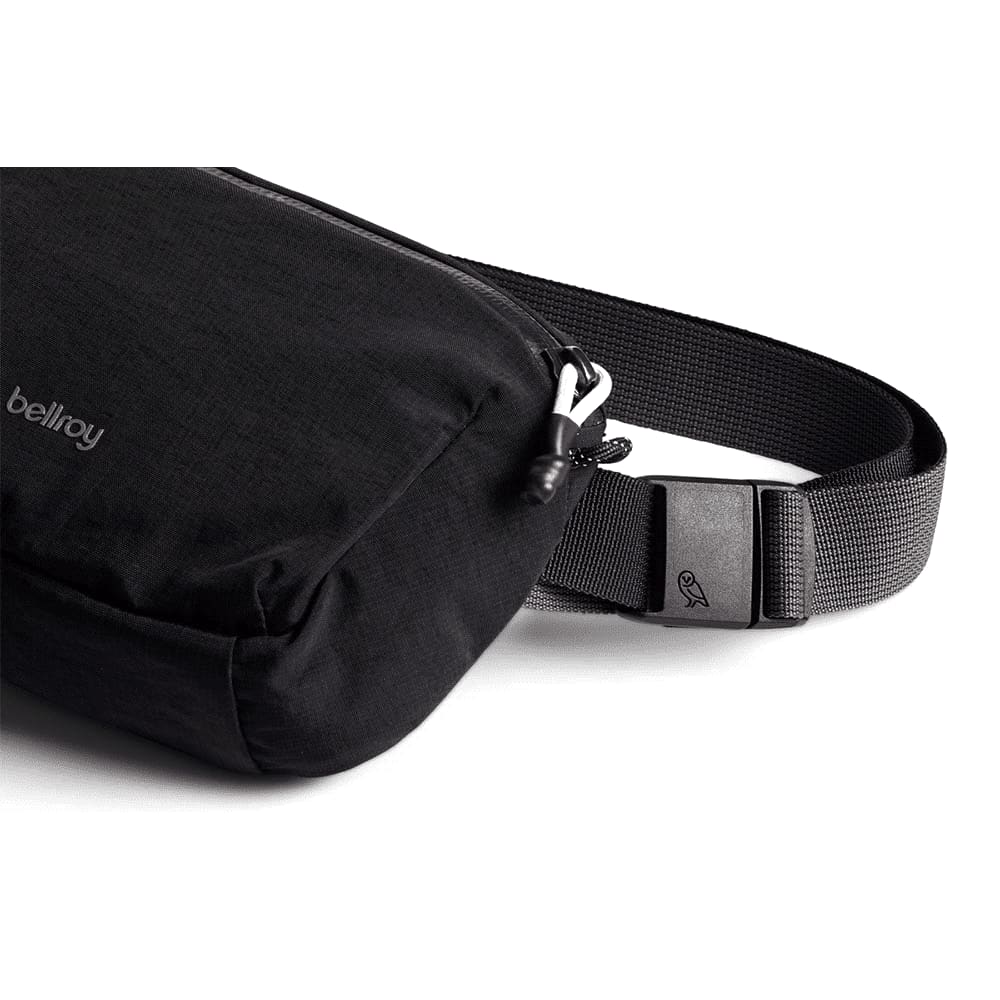 A black Bellroy Lite Belt Bag surrounded by various black items including a phone, sunglasses, and keychain.