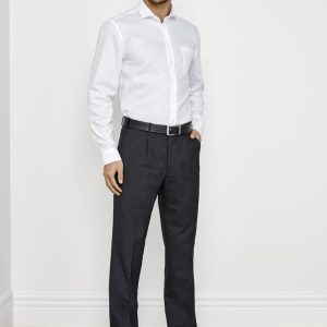 A man wearing a white shirt and dark grey classic pleat pants, standing against a plain wall backdrop.