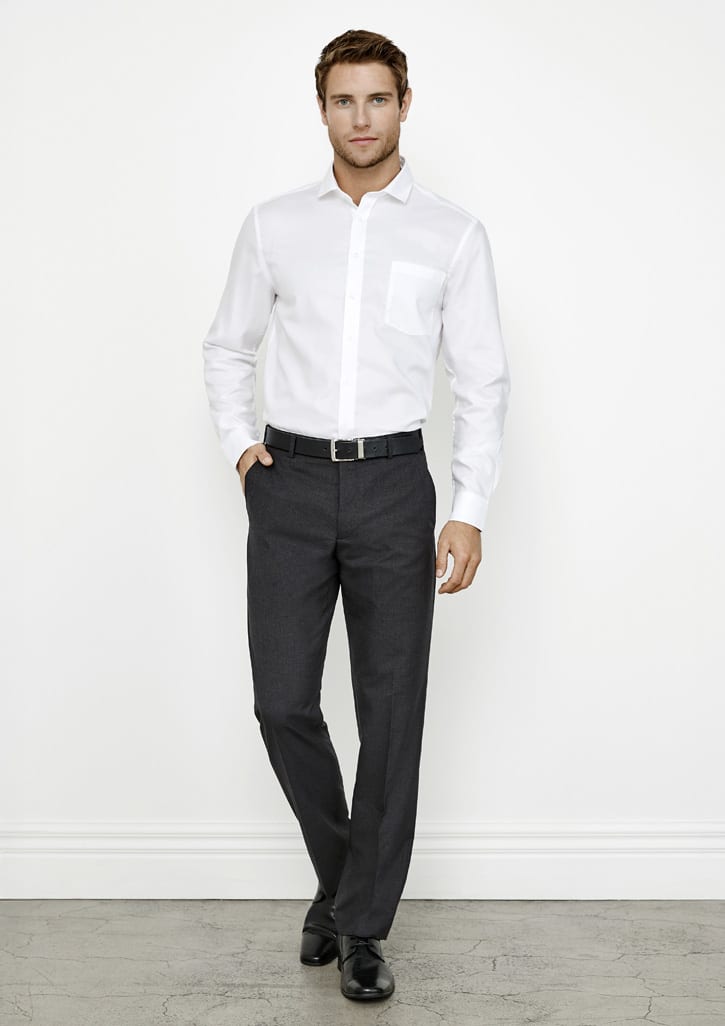A man poses in a white shirt and dark grey classic flat pants, with a belt and sleek shoes, against a plain background.
