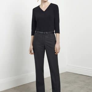 A woman stands wearing black classic pants and a black top, with a belt and stylish heels, set against a light background.