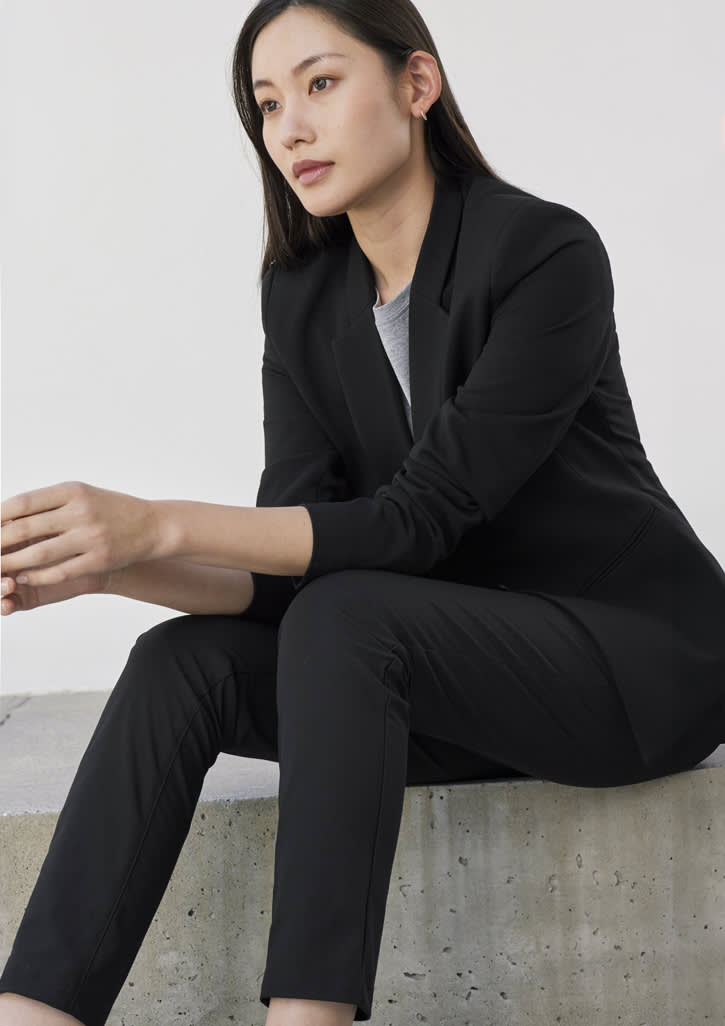 A model wears black Womens Venture Pants paired with a matching blazer, seated against a minimalist backdrop.