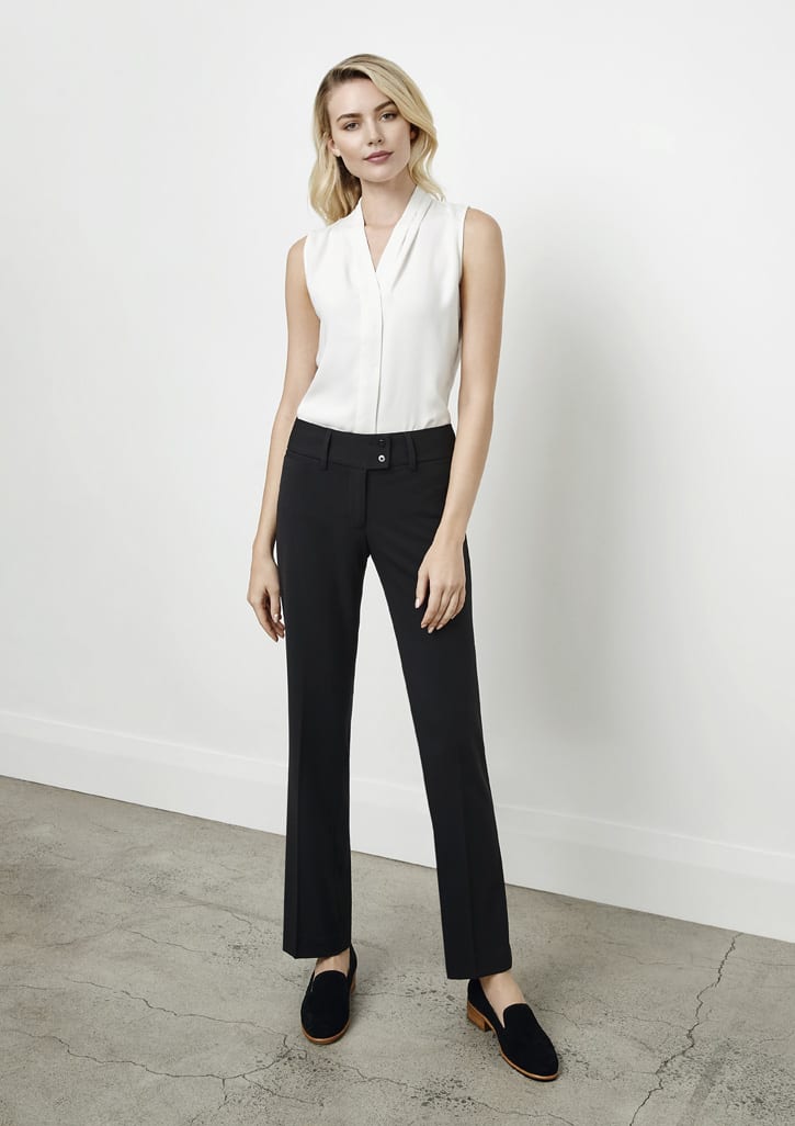 A woman stands in black slacks paired with a white sleeveless top, posed against a neutral background.