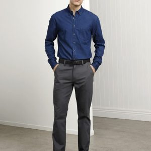 A man stands wearing navy and grey attire, featuring a blue shirt and grey chinos, with a belt and sneakers.