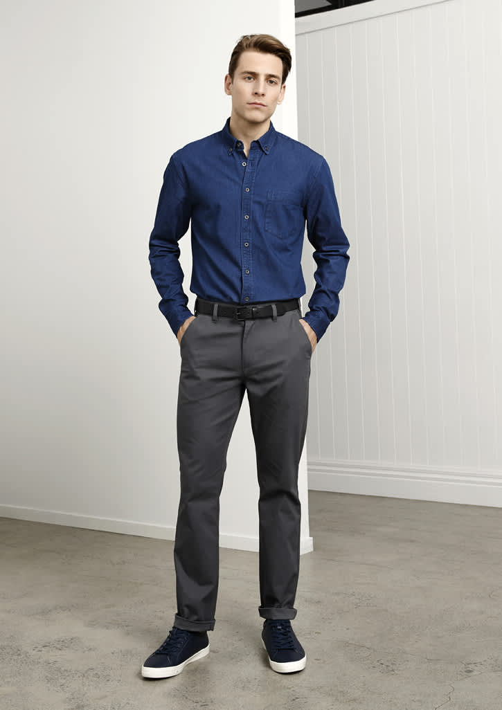 A man stands wearing navy and grey attire, featuring a blue shirt and grey chinos, with a belt and sneakers.