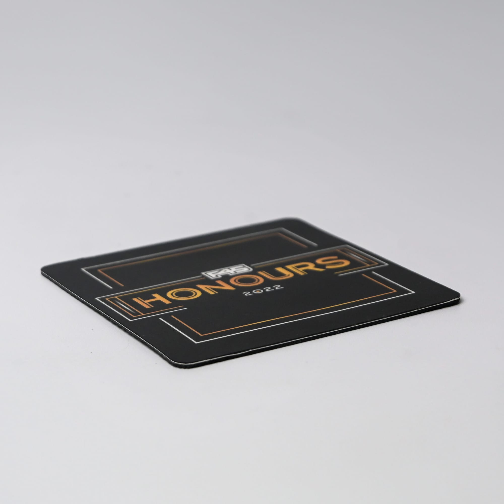 A black deluxe coaster featuring gold accents and a logo, with the word 
