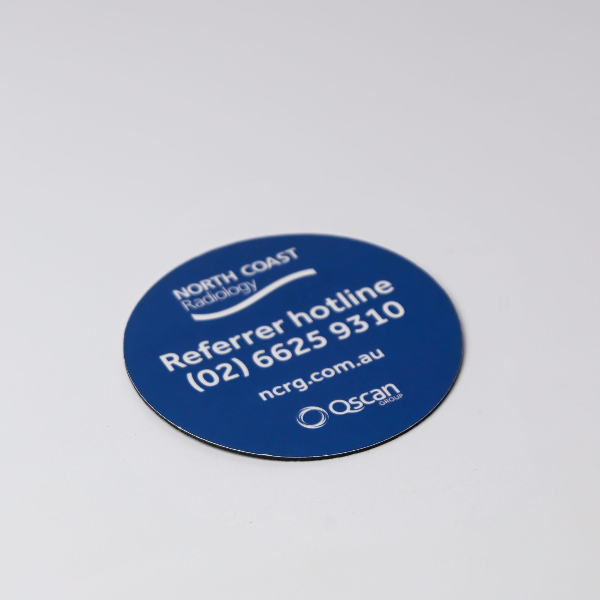 A round, blue coaster featuring a logo and contact information, with a smooth, glossy finish.