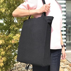 A foldable black calico tote bag with handles, held by a person against a backdrop of greenery.