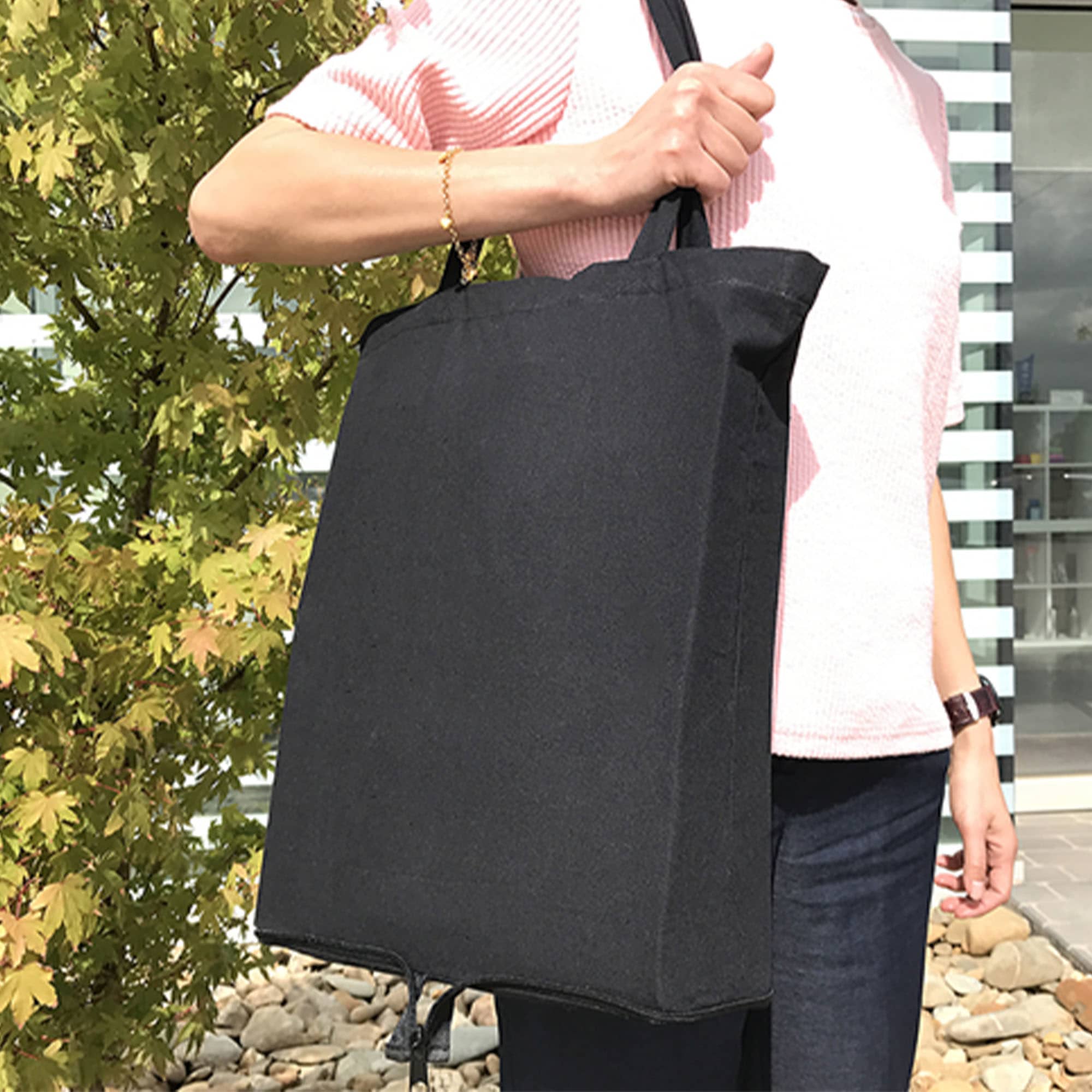 A foldable black calico tote bag with handles, held by a person against a backdrop of greenery.