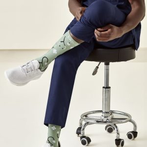 Unisex green socks with a playful design, featuring patterns, worn by a person seated on a stool.