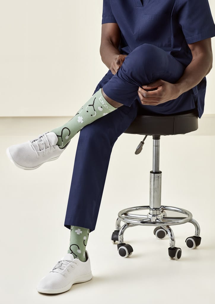Unisex green socks with a playful design, featuring patterns, worn by a person seated on a stool.