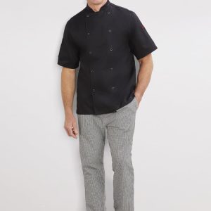 A man stands smiling, wearing a black short-sleeve chef's jacket and grey striped pants with a logo on the jacket.