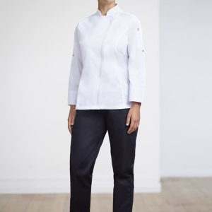 A woman stands wearing a white uniform top and navy scrub bottoms, paired with black shoes, in a bright indoor setting.