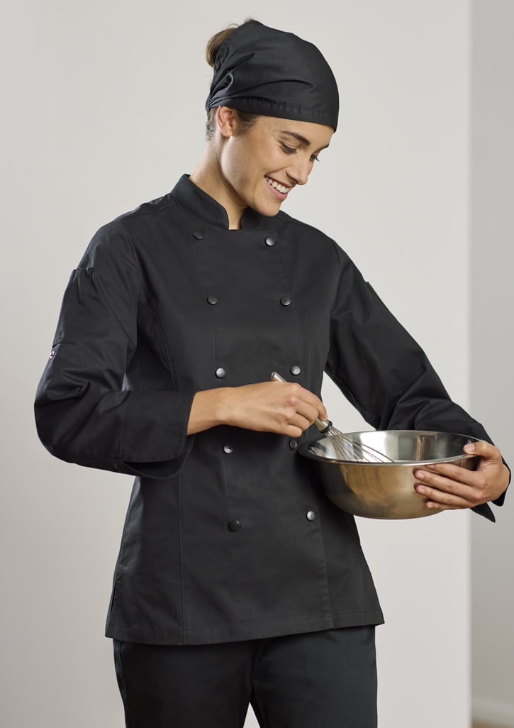 A woman in a black long sleeve chef jacket and matching headband, whisking in a stainless steel bowl.