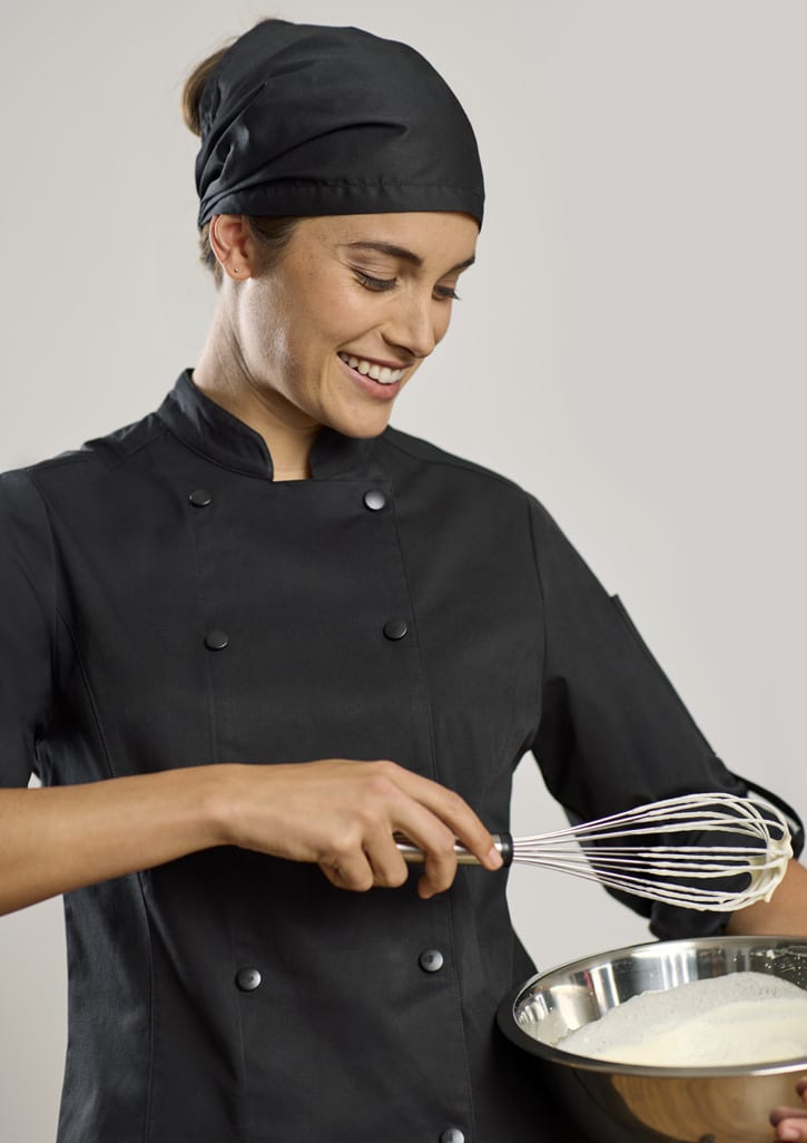 A chef in a black long sleeve jacket and matching headscarf is whisking ingredients in a bowl.