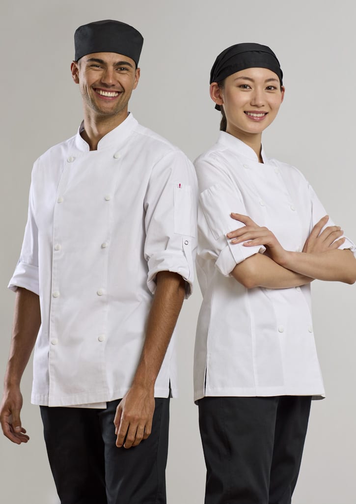 Two chefs stand back-to-back, both wearing white long sleeve chef jackets and black trousers, with one wearing a chef hat and the other a head scarf.