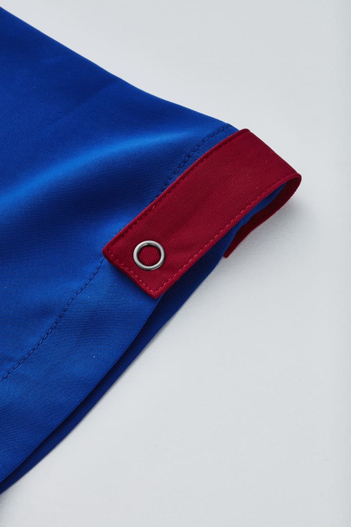 A blue unisex scrub top featuring a red accent and a silver eyelet detail.
