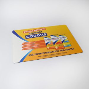 A colourful counter mat featuring a promotional design with products and a logo, highlighting benefits against coughs.