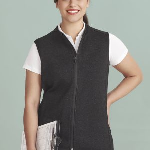 A woman wearing a black vest with a zip front, holding a clipboard, against a light green background.